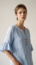 Blouse Capucine bleue à col V et boutons bois, portée par une mannequin, plan taille en studio